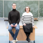 Die Lehrer Kristijan Zrinski und Hildegard Harwix sitzen auf dem Lehrerpult vor der Tafel